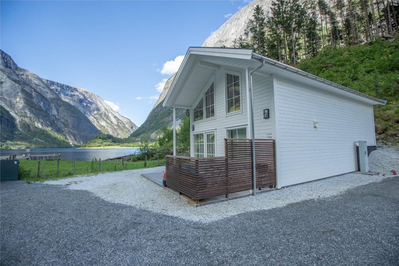 The white cabin at Nærøyfjorden Camping, with the fjord and mountains behind