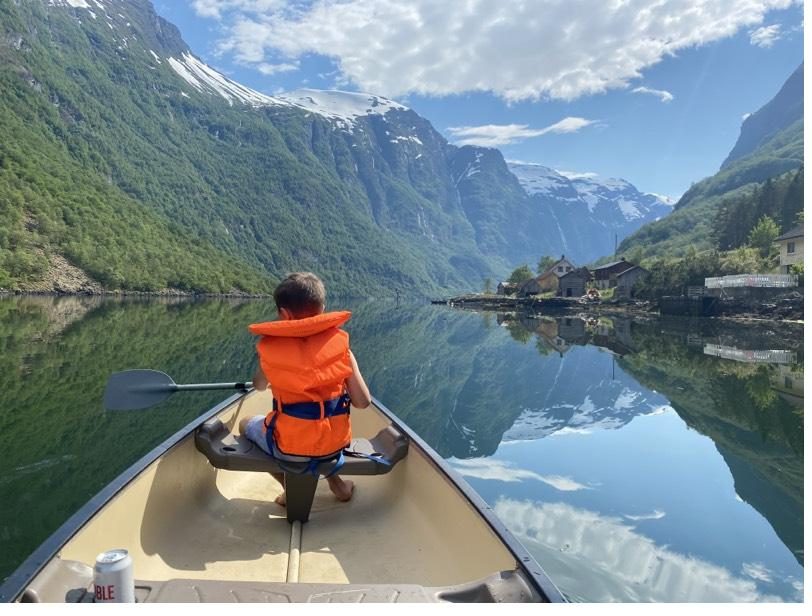 A child in a life jacket paddling one of the camp's canoes on a mirror-calm fjord
