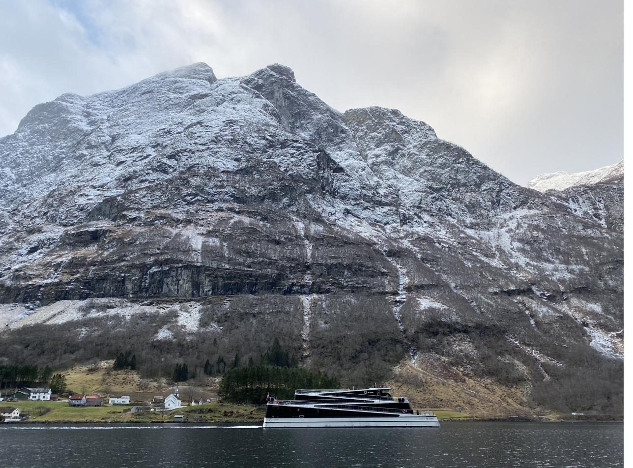An electric sightseeing ship gliding silently past Bakka beneath snow-dusted cliffs
