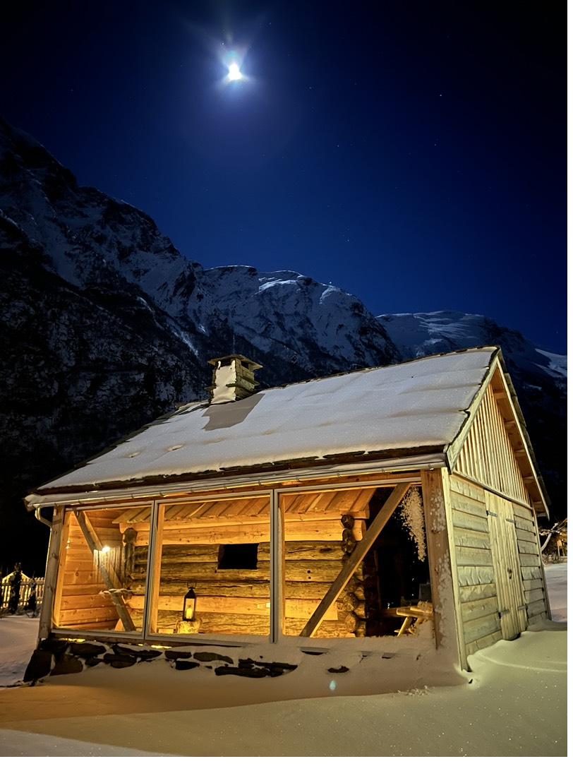 A timber farm building glowing warmly on a snowy winter night in Bakka